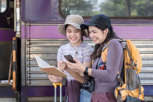 Two Asian female tourist friends are at the train station. Waiting for the train to travel to the provinces together on the weekend..