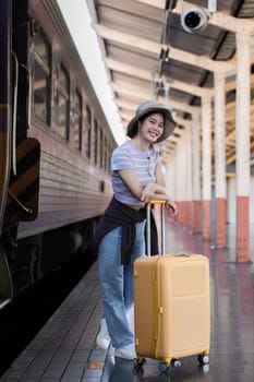 Young woman wearing an explorer's hat and carrying a suitcase Stand and look for a train at the train station. Traveler's concept.