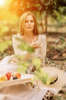 Woman picnic vineyard. Romantic dinner, fruit and wine. Happy woman with a glass of wine at a picnic in the vineyard on sunny day, wine tasting at sunset