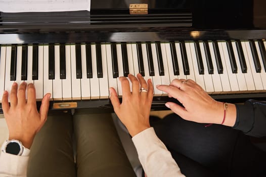 View from above of a young woman with student playing piano, putting fingers on ebony and ivory piano keys. Music lesson. Piano keyboard