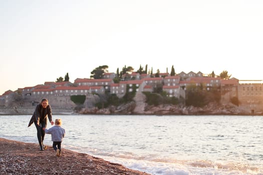 Little girl runs towards her mom along the seashore overlooking the island of Sveti Stefan. Montenegro. High quality photo