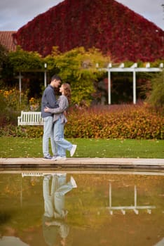 A couple in love hugs on the shore of a city pond in the European town. love story against the backdrop of autumn nature. romantic ambiance, couple goals, outdoor romance, seasonal charm, love in the city, autumnal vibes, European town, city pond, affectionate bonding, love story