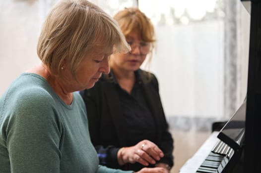 Portrait of two diverse mature women playing piano together at home. Music as therapy.