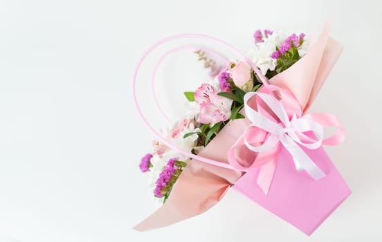 A beautiful bouquet of mixed flowers elegantly wrapped in a box and pink paper and tied with a soft pink ribbon. Among the flowers are roses and lilies, they are fresh and bright