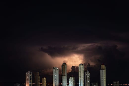 Impressive row of towering skyscrapers with a thunderstorm and lightning bolts above them, perfect for adding text. The buildings dominate the city skyline with their height.