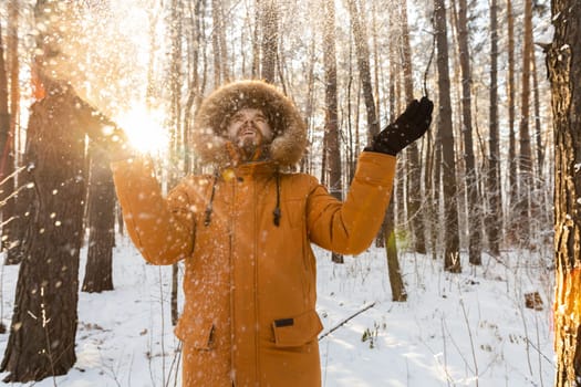 Happy bearded man in hat throws up snow in winter nature. Snowy cold season and holidays lifestyle