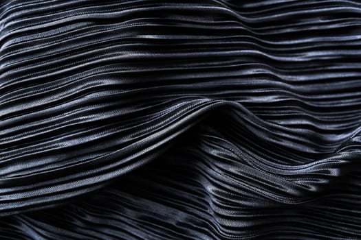 A close-up view of a dark-colored fabric with intricate wavy patterns. The fabric has a glossy finish that reflects light and emphasizes the richness of its color and texture