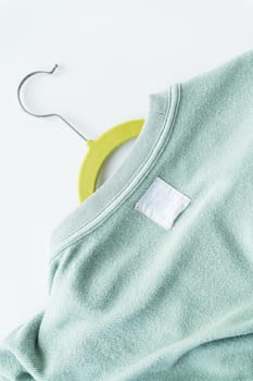 A close-up of a mint green sweater on a yellow hanger. The sweater has a visible texture and a white blank label. The background is plain and white