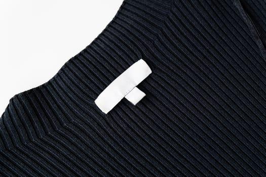 A black ribbed fabric garment with a white blank clothing label stitched onto it. The label is empty with no text or logo