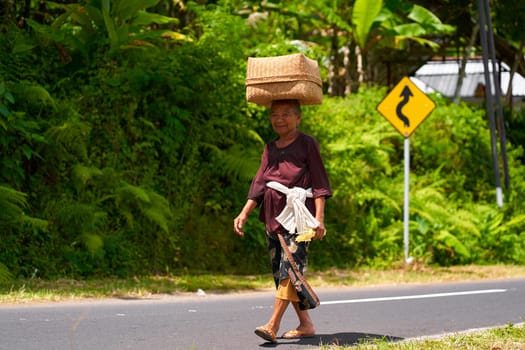 Local women carry baskets of food on their heads in an Indonesian village. Portrait of a smiling woman in Bali. Bali, Indonesia - 12.10.2022