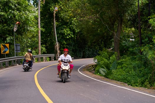 A person on a motorcycle rides a scenic asphalt road in Asia. Bali, Indonesia - 12.10.2022