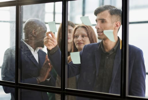 Creative business team looking at sticky notes on glass window