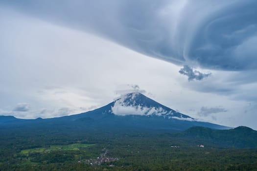 Panorama of Mount Agung and rice fields on the island of Bali. View of the mountain against a background of palm trees and a cornfield. Panorama of Agung volcano covered with clouds on a rainy day