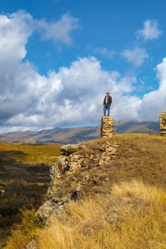 A lone man stands on the crumbling fortress wall, gazing out at the magnificent mountain range, engulfed by the grandeur of the scenic view before him.