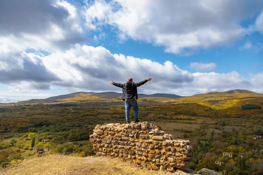 Man standing on a crumbling fortress wall, gazing at a stunning mountain vista. Awe-inspiring contrast between the ancient wall and the majestic mountains.