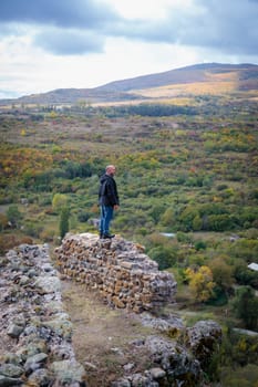 A lone figure stands at the edge of ancient mountain fortress ruins, overlooking the vast and majestic scenery below, evoking a powerful sense of solitude and contemplation in this solitary moment.