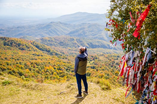 A man stands at the sacred viewpoint in the mountains, basking in the tranquil beauty of the landscape. The serene atmosphere and vast expanse of nature create a peaceful and awe-inspiring scene.