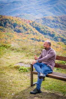 A man sits peacefully, finding solace in the serene and breathtaking view of a sacred mountain peak and its majestic natural landscape, providing a perfect setting for meditation and tranquility.