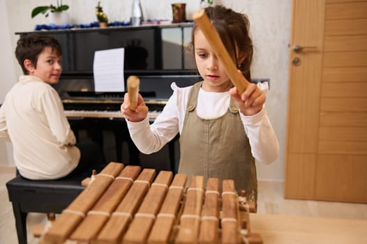 Adorable teenage boy and little girl enjoy playing together on musical instruments, performing melody on xylophone and piano. Kids education and entertainment, Music lovers. Childhood, Education