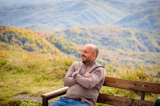 The image conveys a profound connection with nature as a man rests on a wooden bench, taking in the breathtaking view of the mountain range, evoking a sense of wonder and tranquility.