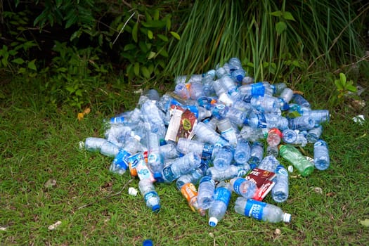 A pile of empty plastic bottles thrown away by tourists in the grass. The problem of ecology and human pollution. Bali, Indonesia - 01.01.2023