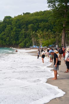 A crowd of tourists walks and takes pictures on a tropical beach. Bali, Indonesia - 12.30.2022