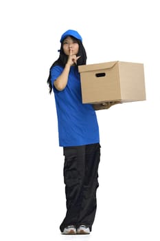 The delivery girl, on a white background, full-length, with a box, shows a sign of silence.