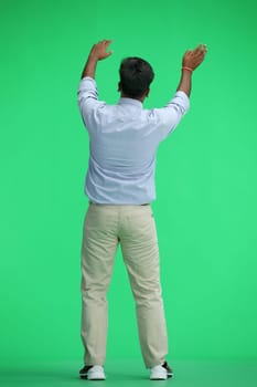 A man in a blue shirt, on a green background, standing tall, waving his arms, back view.