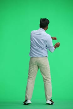 A man in a blue shirt, on a green background, standing tall, waving his arms, back view.