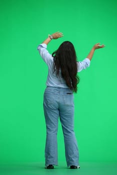 A girl in a blue shirt, on a green background, in full height, waving her arms, back view.