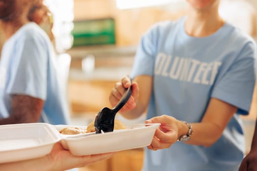 At charitable food drive, caucasian lady is shown offering a warm meal to a disadvantaged hungry homeless person. A close-up of a team of humanitarian relief workers distributing free food.