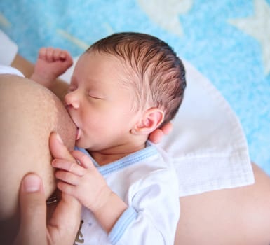 Close-up view of adorable newborn baby boy suckling at mother's breast. Cropped view of unrecognizable mother breastfeeding her child