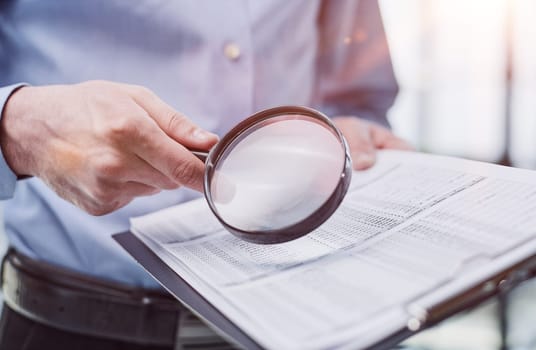 man looking through a magnifying glass to documents notebook.