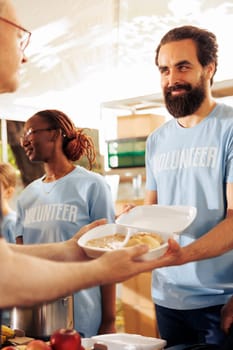 A diverse group provides humanitarian aid at a community center, distributing free food to the homeless. Multiracial volunteers collaborate to support the underprivileged and organize food drives.