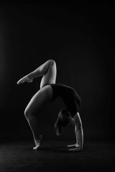 Flexible girl, rhythmic gymnastic artist jumping on white dark background. Grace in motion, action.