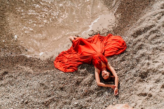 Woman red dress sea. Female dancer in a long red dress posing on a beach with rocks on sunny day.