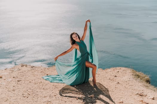 Woman green dress sea. Female dancer posing on a rocky outcrop high above the sea. Girl on the nature on blue sky background. Fashion photo