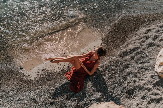 Woman red dress sea. Female dancer in a long red dress posing on a beach with rocks on sunny day.