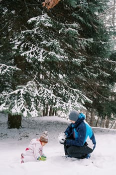 Little girl and dad making snowballs while squatting in a snowy forest. High quality photo