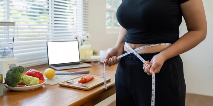 overweight Asian woman measuring her hip while learning to make salad and healthy food from social media.