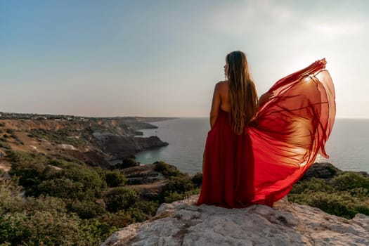 Woman sunset sea red dress, back view a happy beautiful sensual woman in a red long dress posing on a rock high above the sea on sunset