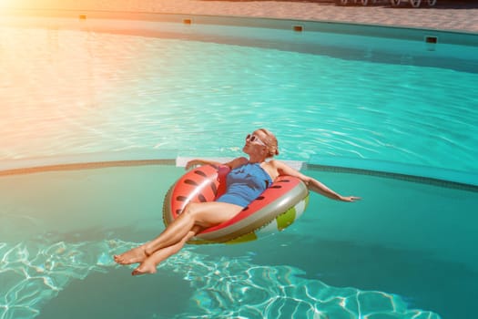 Happy woman in a swimsuit and sunglasses floating on an inflatable ring in the form of a watermelon, in the pool during summer holidays and vacations. Summer concept