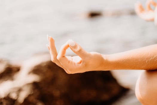 Yoga on the beach. A happy woman meditating in a yoga pose on the beach, surrounded by the ocean and rock mountains, promoting a healthy lifestyle outdoors in nature, and inspiring fitness concept