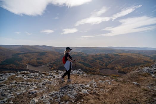 woman on mountain peak looking in beautiful mountain valley in autumn. Landscape with sporty young woman, blu sky in fall. Hiking. Nature.