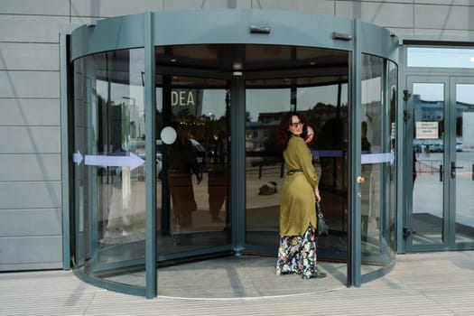 woman entering a supermarket. Caucasian model with long brunette hair, wears sunglasses and a khaki dress