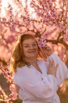 Woman blooming peach orchard. Against the backdrop of a picturesque peach orchard, a woman in a long white dress enjoys a peaceful walk in the park, surrounded by the beauty of nature