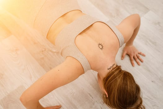 Top view of a muscular woman during push-ups. She is wearing a beige top and leggings, with a round tattoo between her shoulder blades. The concept of a healthy lifestyle