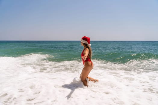 A woman in Santa hat on the seashore, dressed in a red swimsuit. New Year's celebration in a hot country