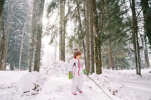 Little girl with a stick in her hand stands in a snowy forest and looks away. High quality photo