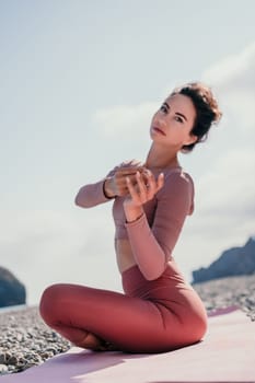 Young woman with long hair in white swimsuit and boho style braclets practicing outdoors on yoga mat by the sea on a sunset. Women's yoga fitness routine. Healthy lifestyle, harmony and meditation